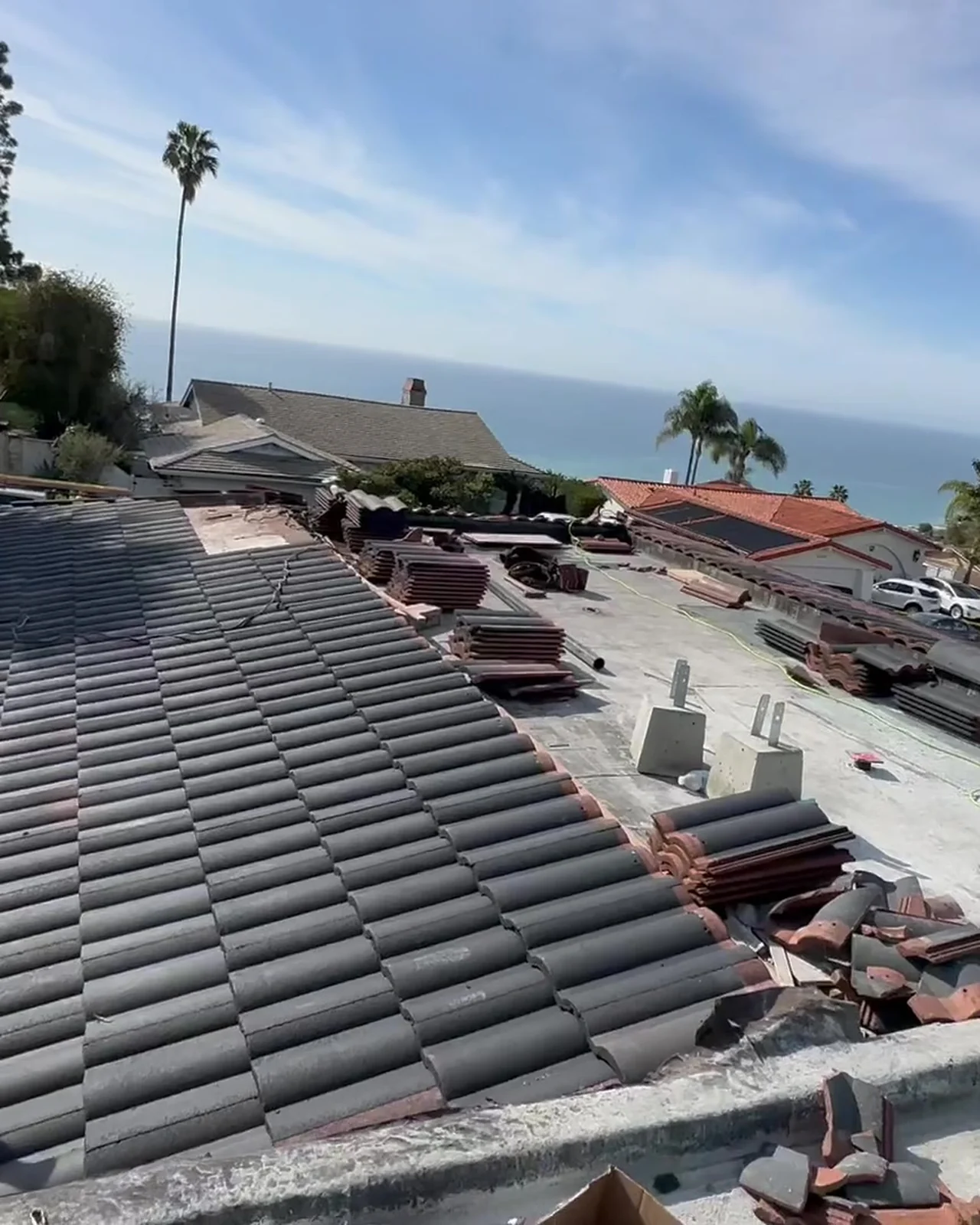 Clay tiles lifted off and set down in rows across the opened deck, the water visible past the palms