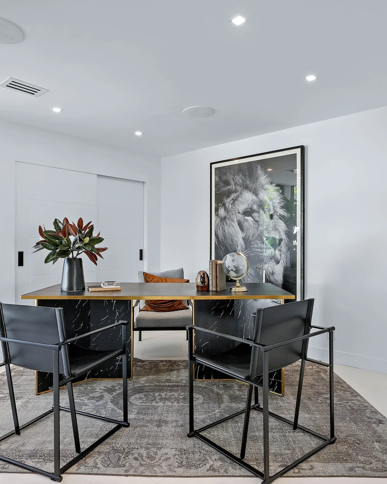 Rebuilt dining room with a black steel-frame table, black leather sling chairs, an oversized black-and-white photograph, pale flooring and a patterned rug