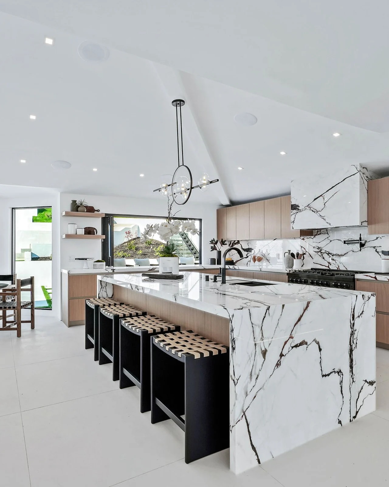 The new kitchen under a pitched white ceiling, its island wrapped in mirrored stone that folds over both ends, black bench seating and flush-set appliances behind oak fronts