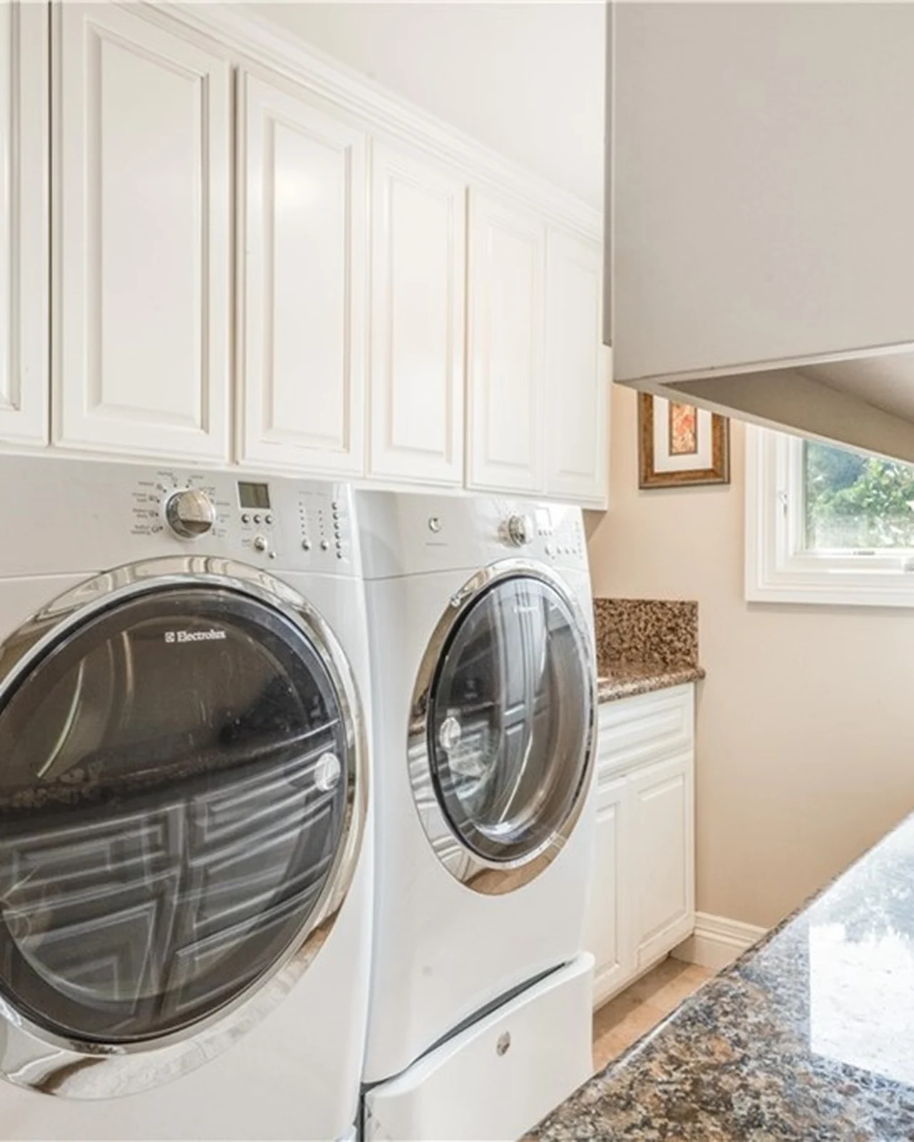 Original laundry room with white raised-panel upper cabinets, a speckled granite counter, a front-load washer and dryer and beige walls