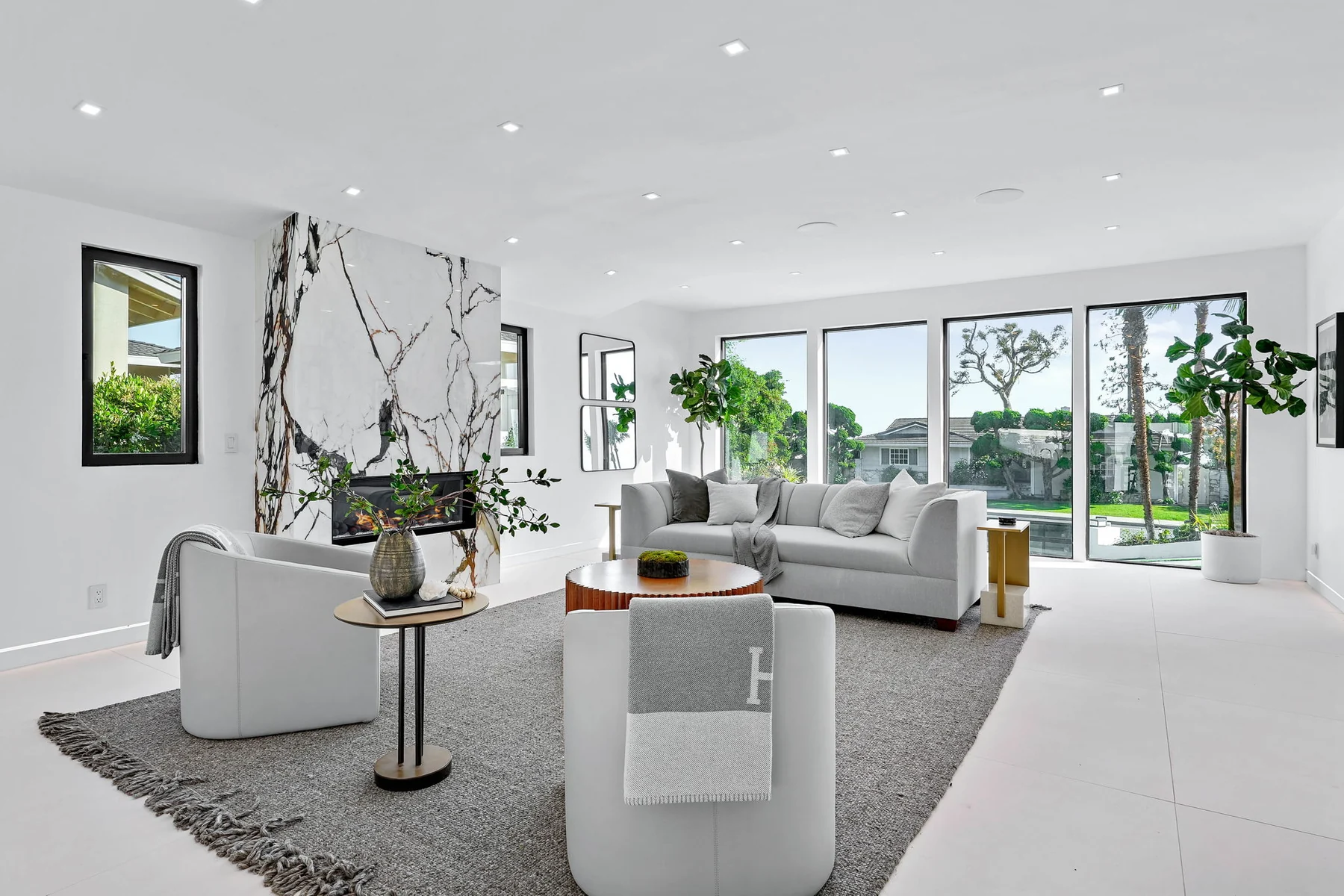 Wide view of the living room with the veined marble slab fireplace wall, linear fire and low seating