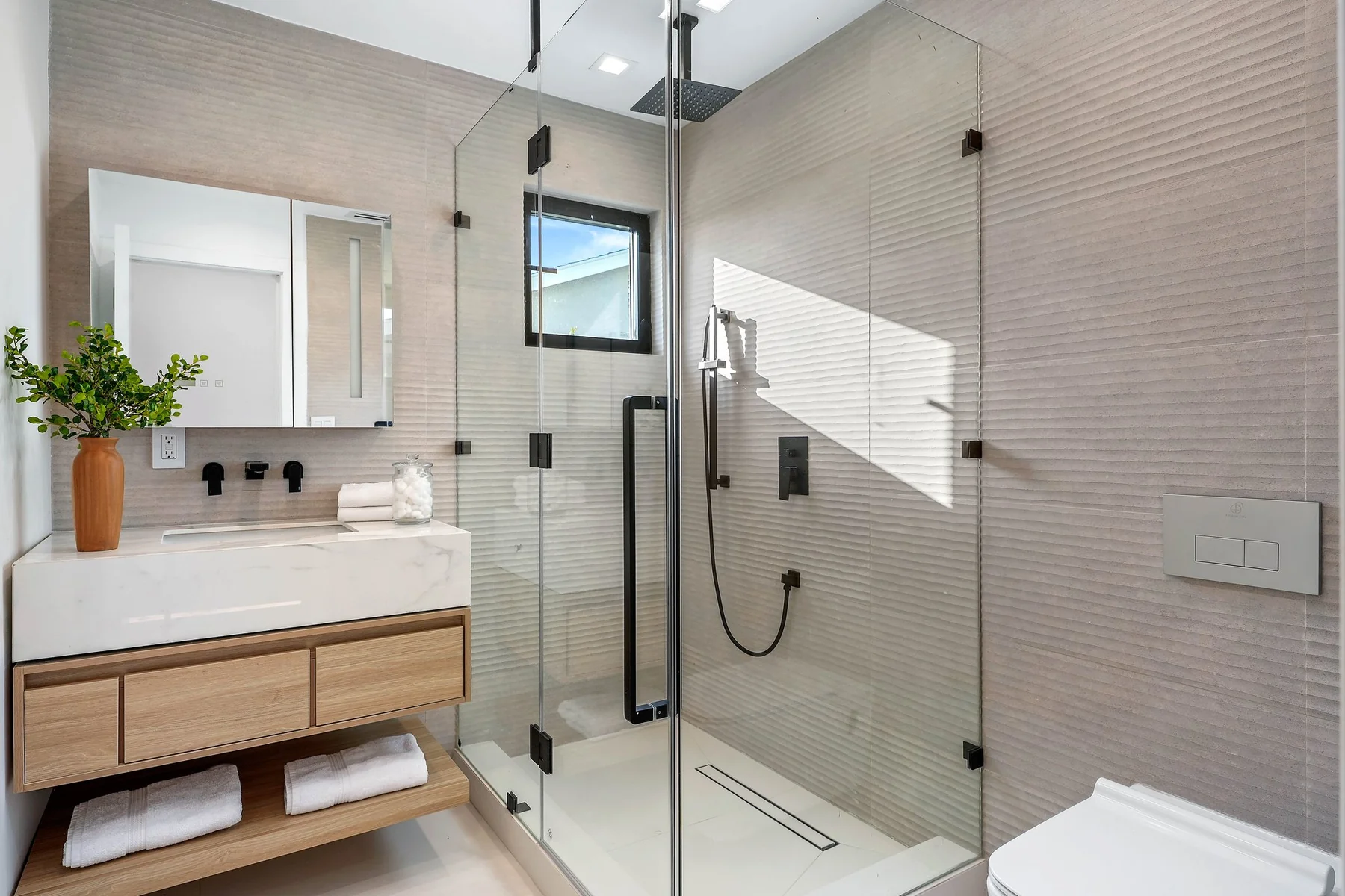 White oak floating vanity with an integrated mirror and a walk-in shower alongside