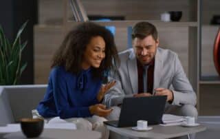 Mulher de negócios explica sobre a gestão de contratos a seu colega executivo enquanto eles analisam informações no computador à sua frente.