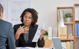 Mulher em escritório segurando relatório e explicando ao seu colega como a receita recorrente favorece a maximização de lucro.