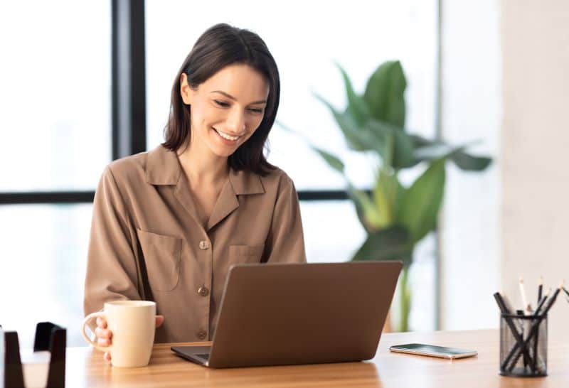 Mulher sorridente em escritório feliz por não precisar usar planilha de contas a pagar.