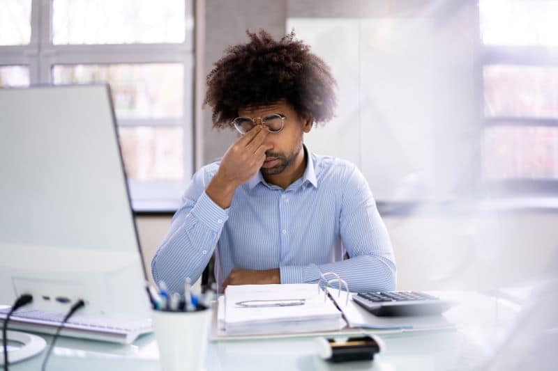 Gestor contábil sentado em frente ao computador e com a mão no rosto, preocupado, pensando como diminuir a inadimplência.