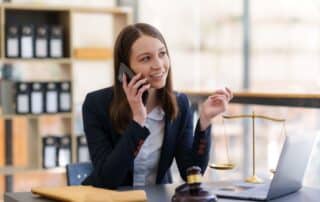 advogada falando com cliente no celular enquanto trabalha em sua mesa, com computador e decorações relacionadas à advocacia