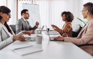 Equipe de gestores em reunião conversando sobre escalabilidade dos negócios, em mesa com computadores e documentos.