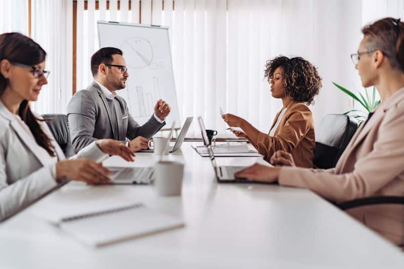 Equipe de gestores em reunião conversando sobre escalabilidade dos negócios, em mesa com computadores e documentos.