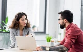 Sócios de associação conversam sobre automatização de processos enquanto visualizam tudo no computador em cima da mesa.