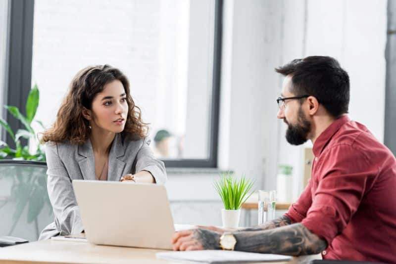 Sócios de associação conversam sobre automatização de processos enquanto visualizam tudo no computador em cima da mesa.