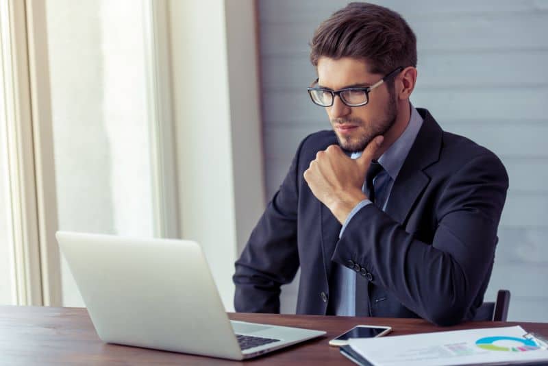 homem de terno trabalha em seu escritório olhando o computador, com gráficos impressos ao seu lado