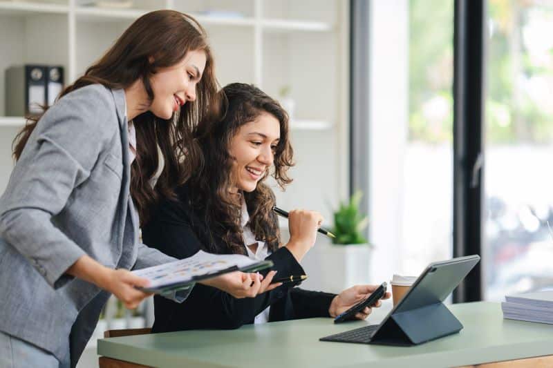 Duas gestoras conversam sobre o CAC enquanto analisam dados em tablet.