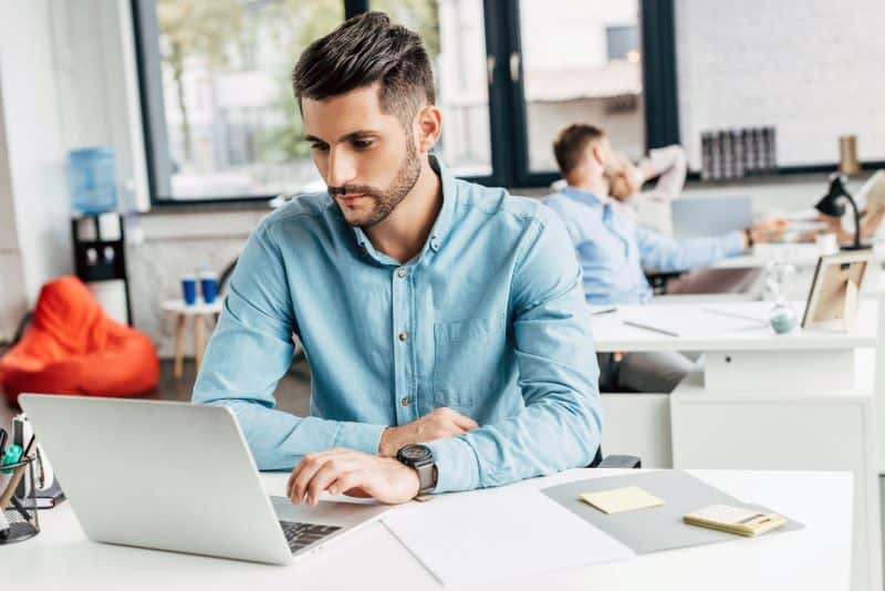 Homem em escritório lendo no notebook sobre como calcular juros e multa de forma automática.