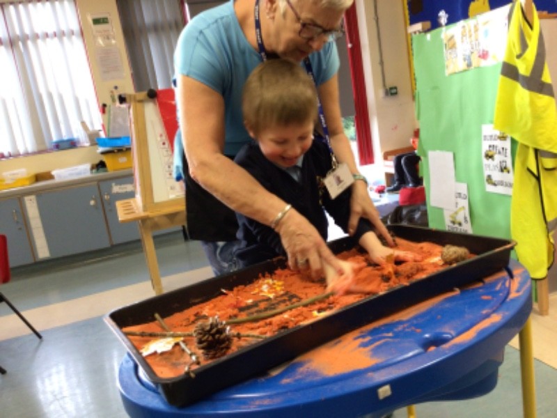 I am being encouraged to enjoy sensory mark making in the seasonal sand tray.