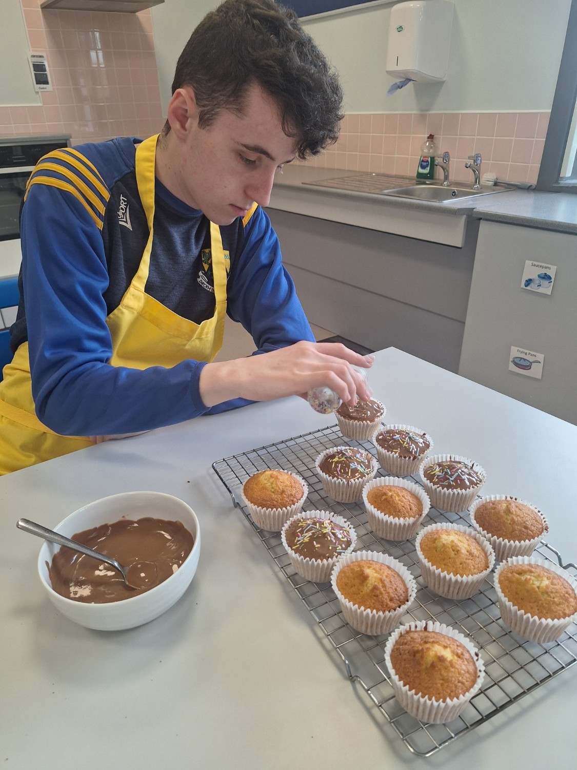 Dylan is decorating his muffins with chocolate and sprinkles.