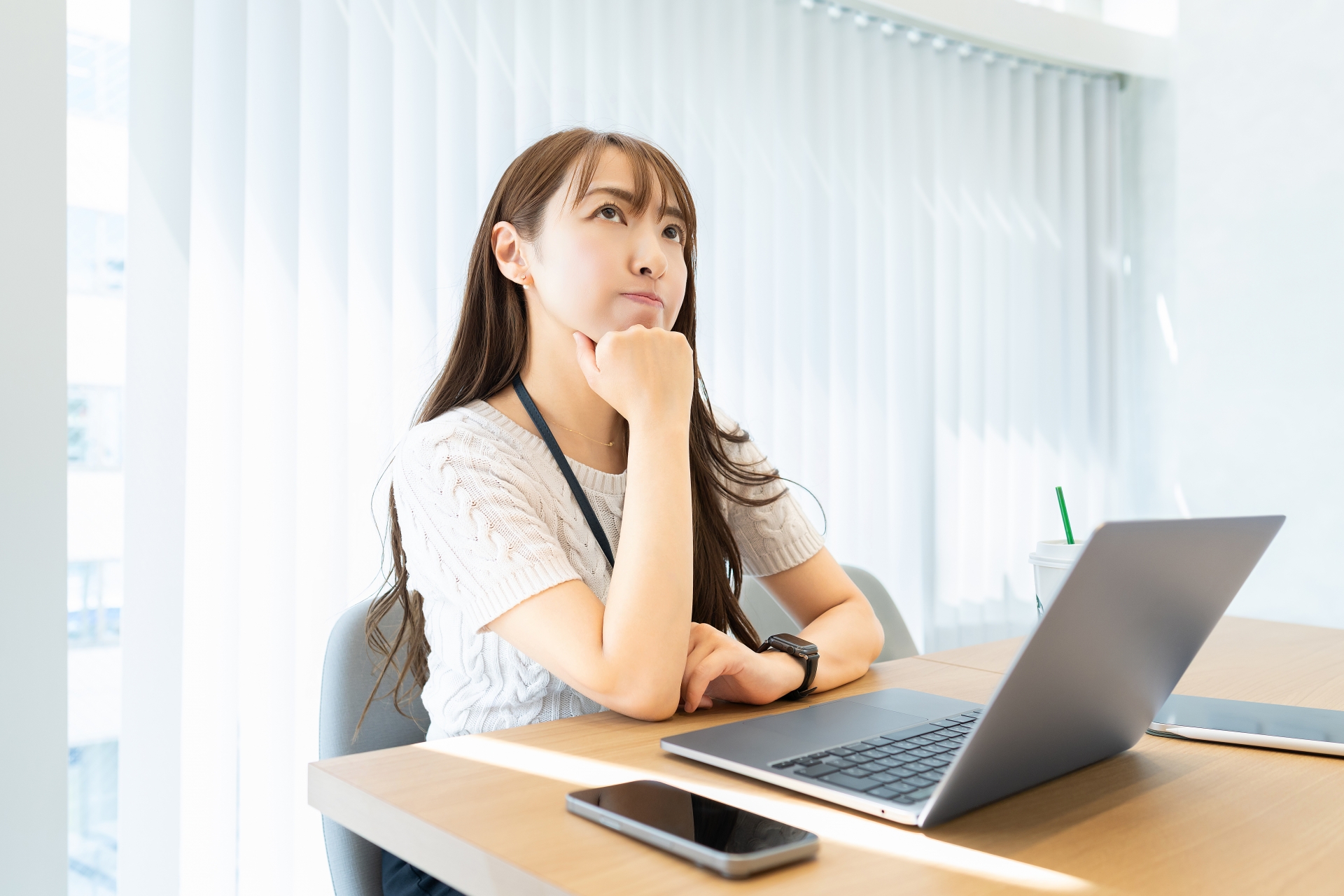 ノートPCが置かれたテーブルで、白い服を着た女性が顎に手を当てて斜め上を見つめ、考え込んでいる表情。ヒューリスティック分析が自社のような小規模サイトでも効果があるのか疑問に感じている。