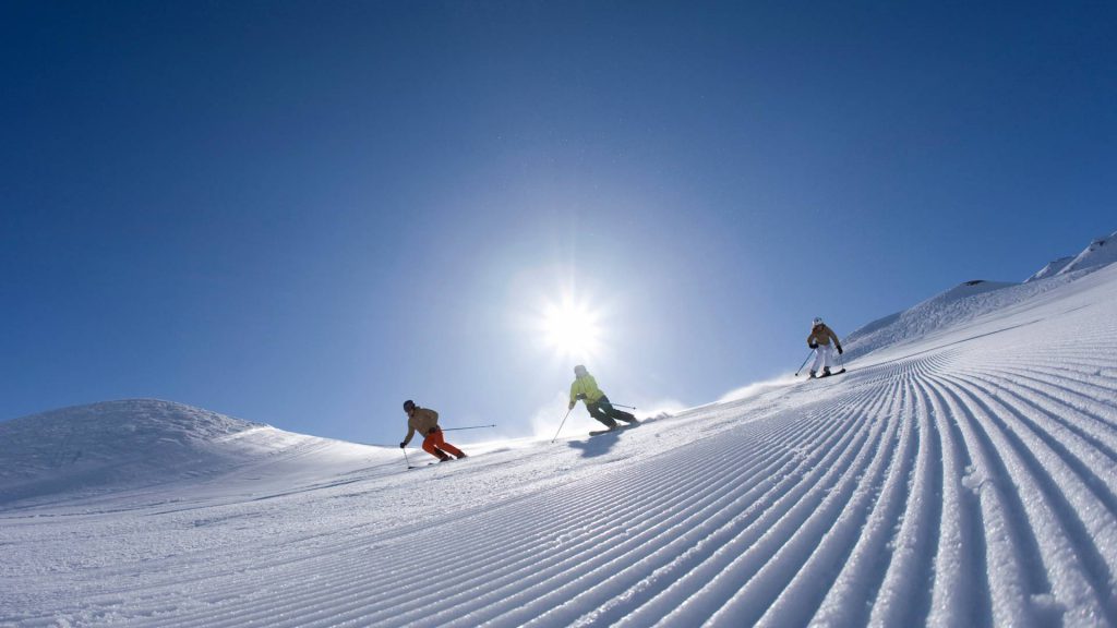 three skiers enjoy freshly groomed piste in the sun