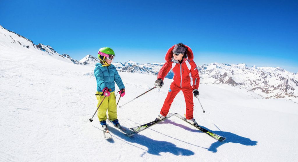 private ski instructor in red ski suit gives tips to child in kids private ski lesson