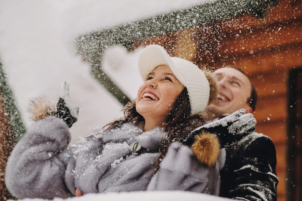 Stylish couple playing with snow in wooden cabin on background of winter snowy mountains