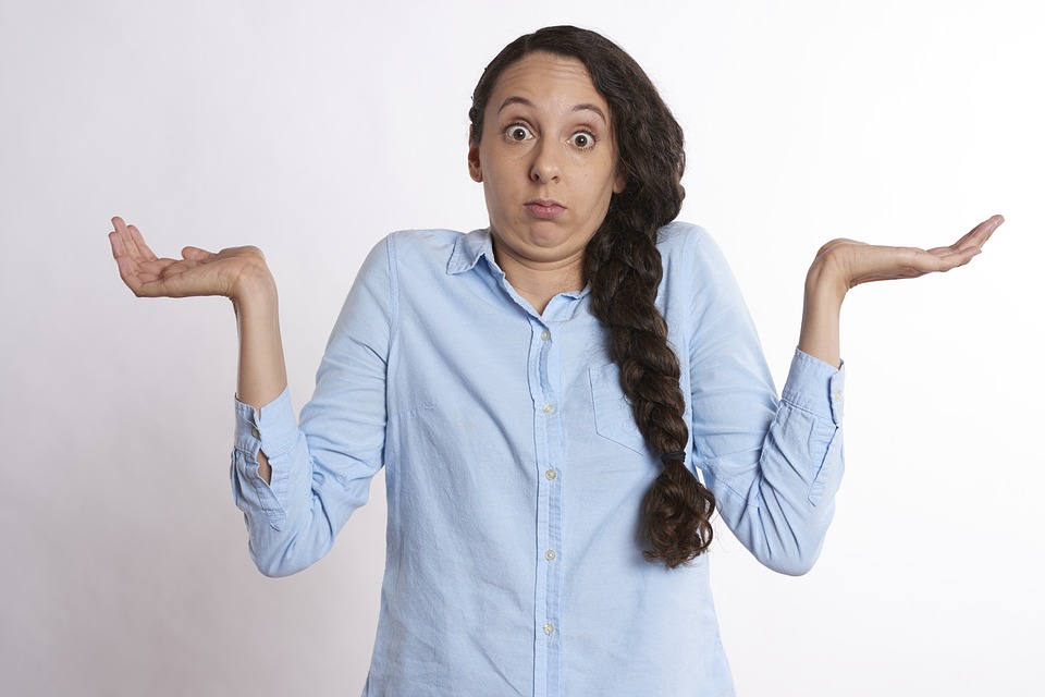 confused woman in blue dress shirt shurgging