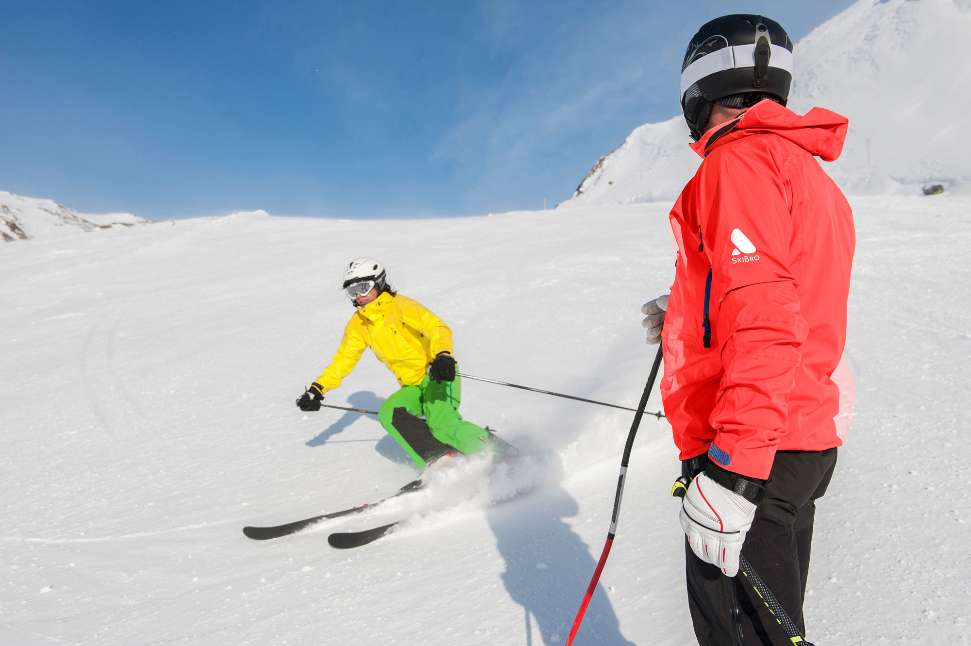 ski instructor in red jacket watches student carve on ski run