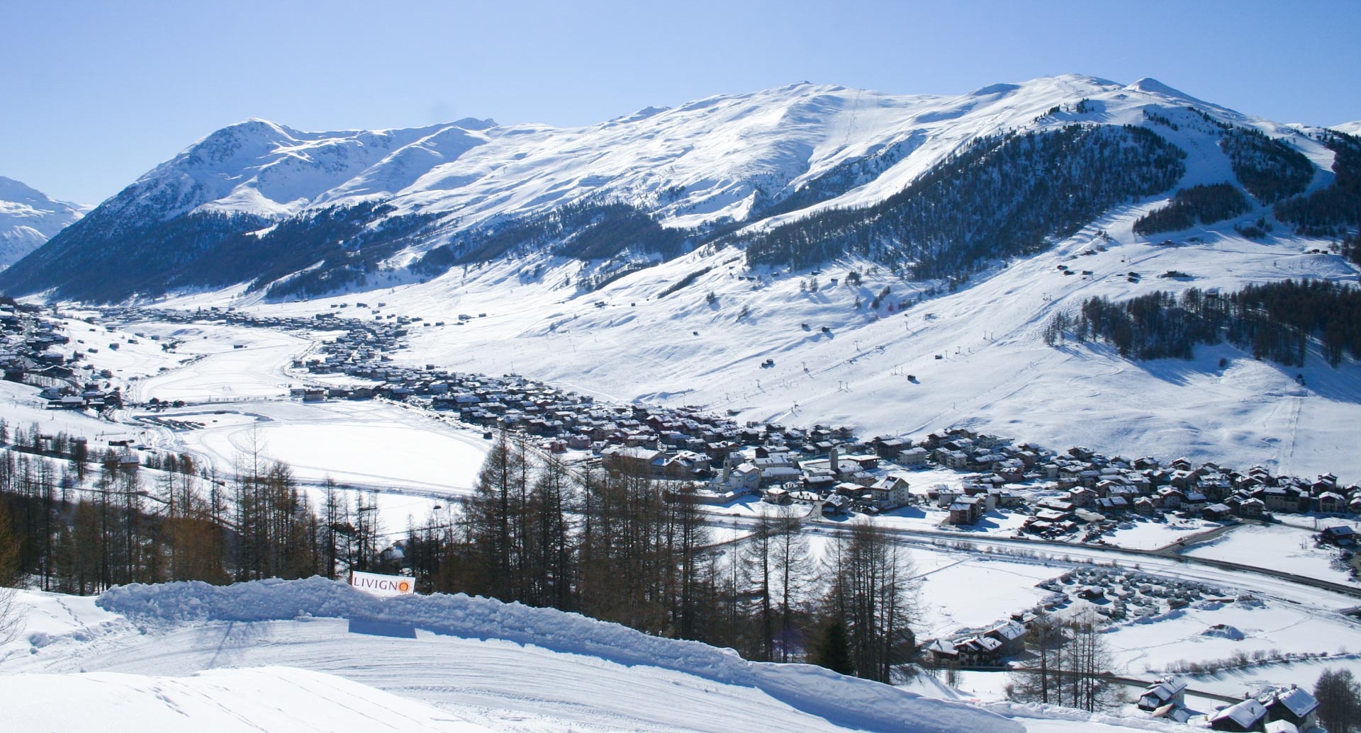 The village of Livigno nestled in underneath the tree-lined ski slopes of the mountains above.