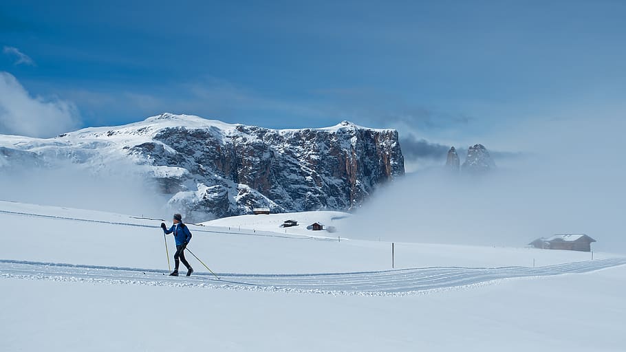 Woman in blue cross-country skiing in front of mountains and low clouds