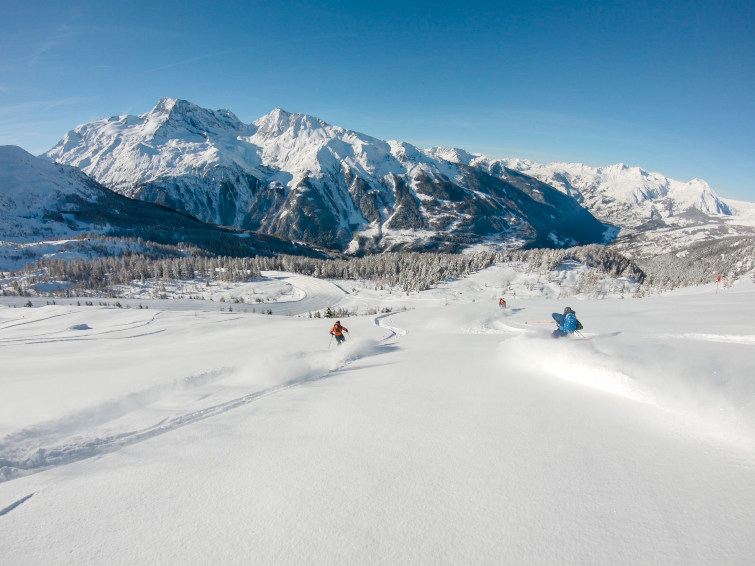 Two skiers ski through a field of powder towards a large mountain in Ste Foy