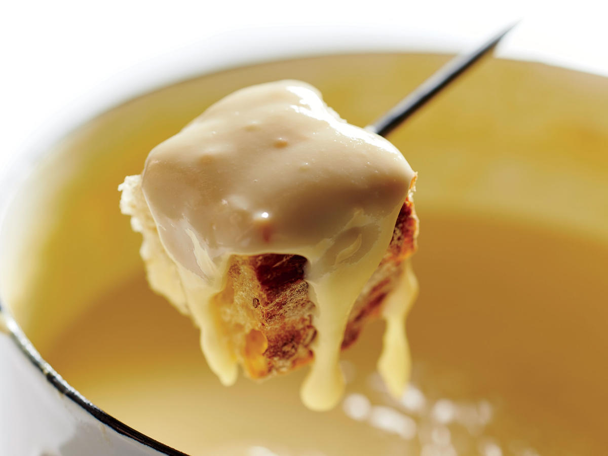 A close up of a piece of bread dripping with cheese fondue