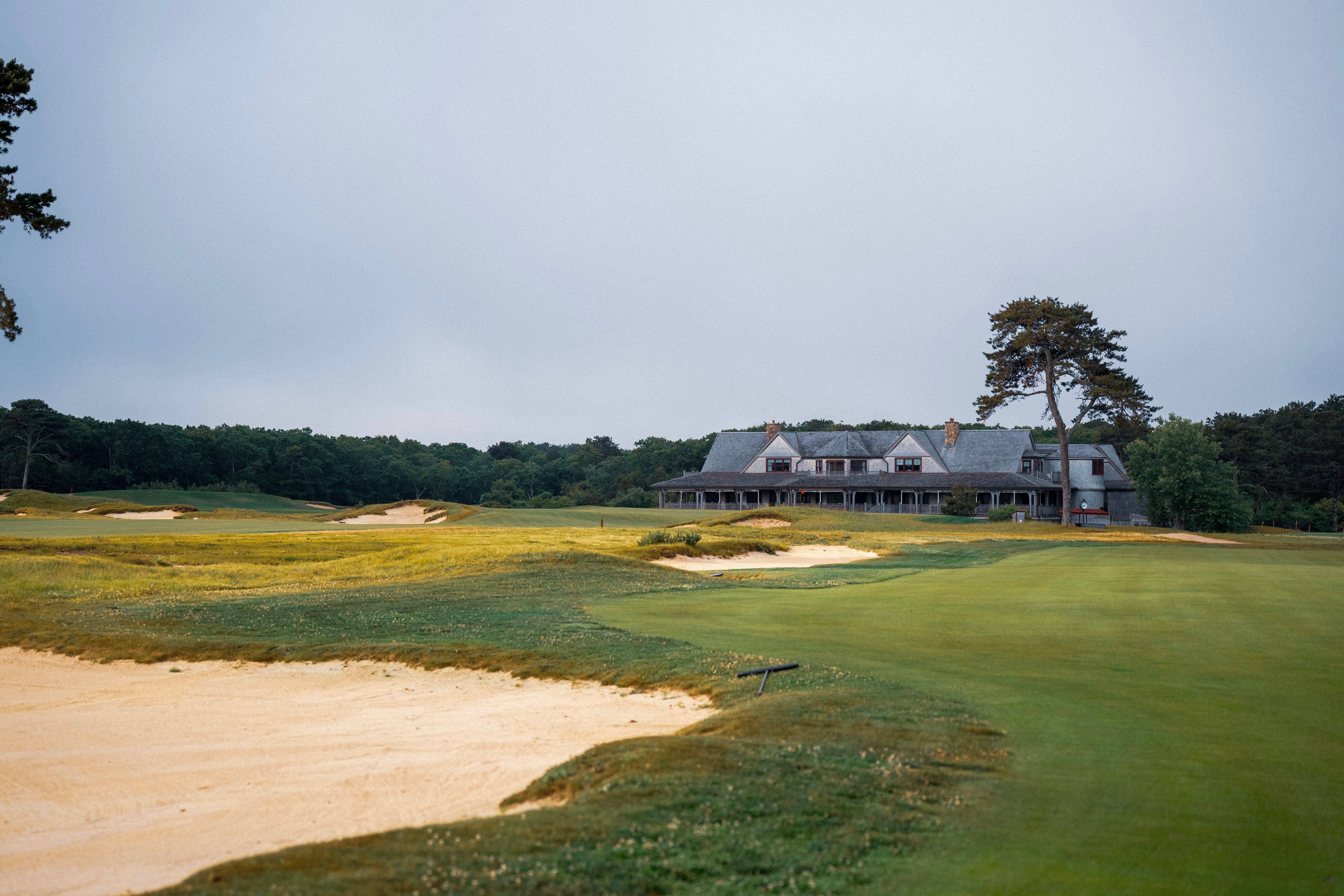 Lush green golf course with a prominent sand trap leading to a distant clubhouse.