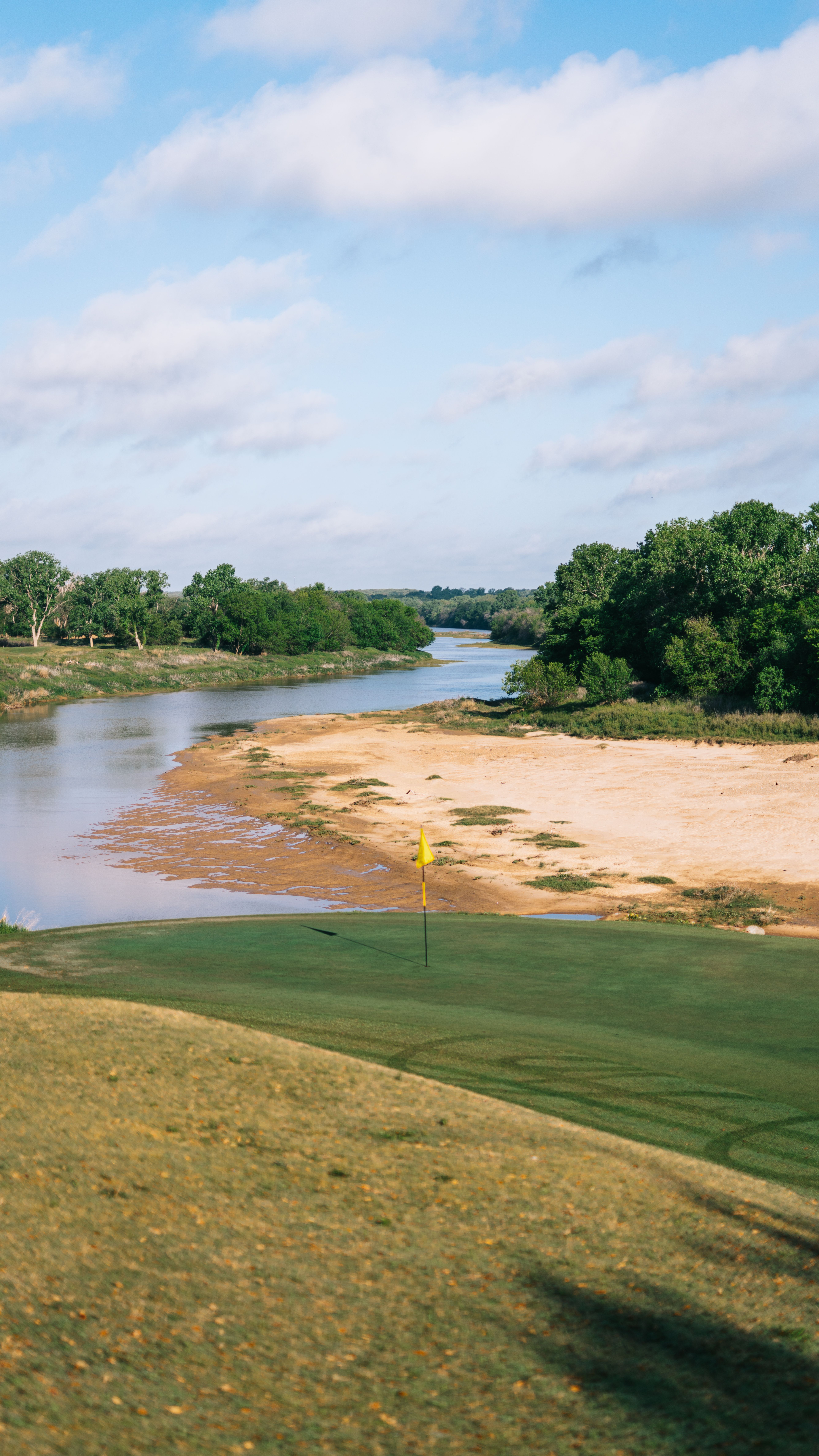 Winding river flows past a sandy bank and green landscape under a blue sky.