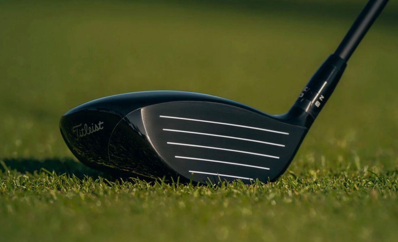 Close-up of a black golf club head with grooves resting on vibrant green grass.