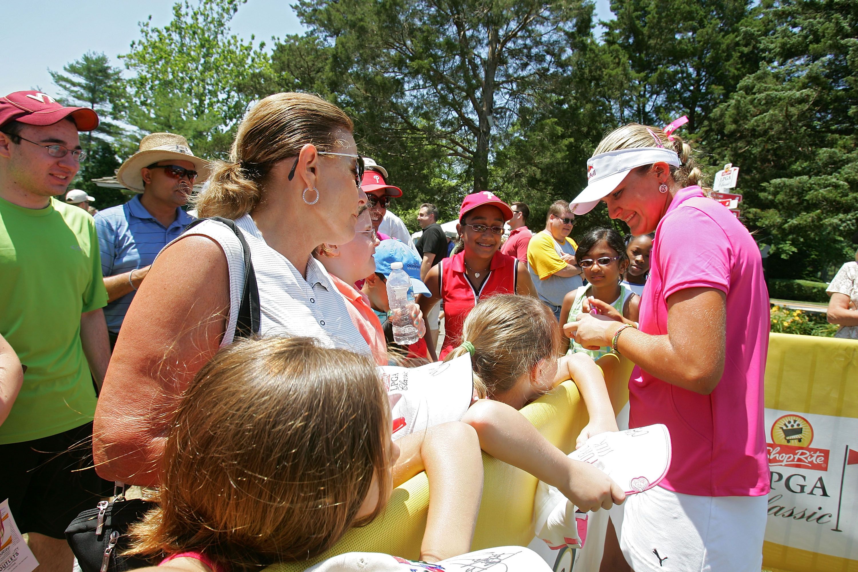Woman in pink shirt and visor interacts with a child at an outdoor event.