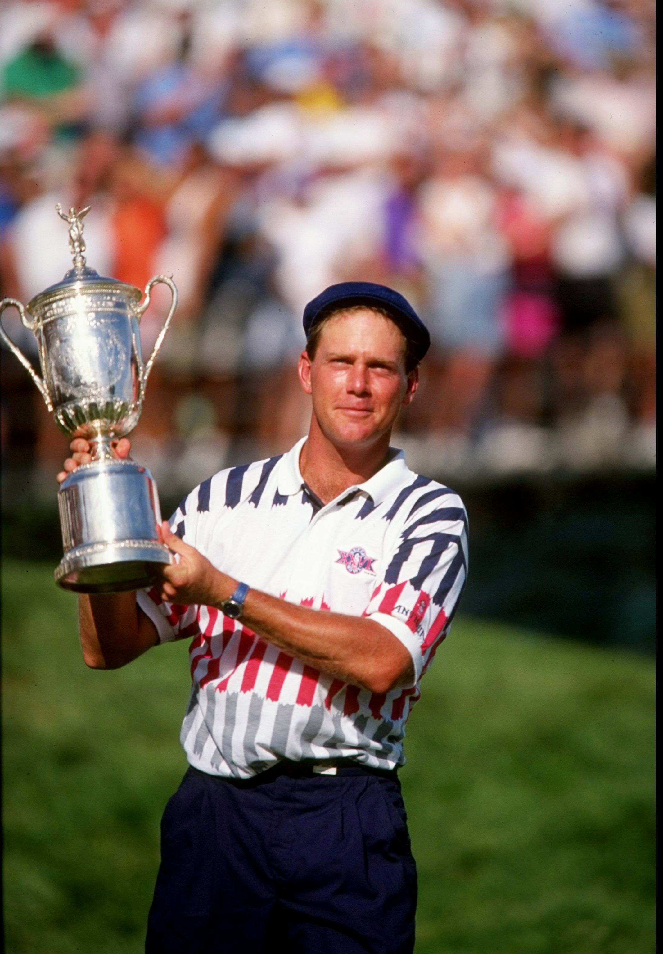 Golfer Payne Stewart triumphantly holds the U.S. Open trophy on a green course.