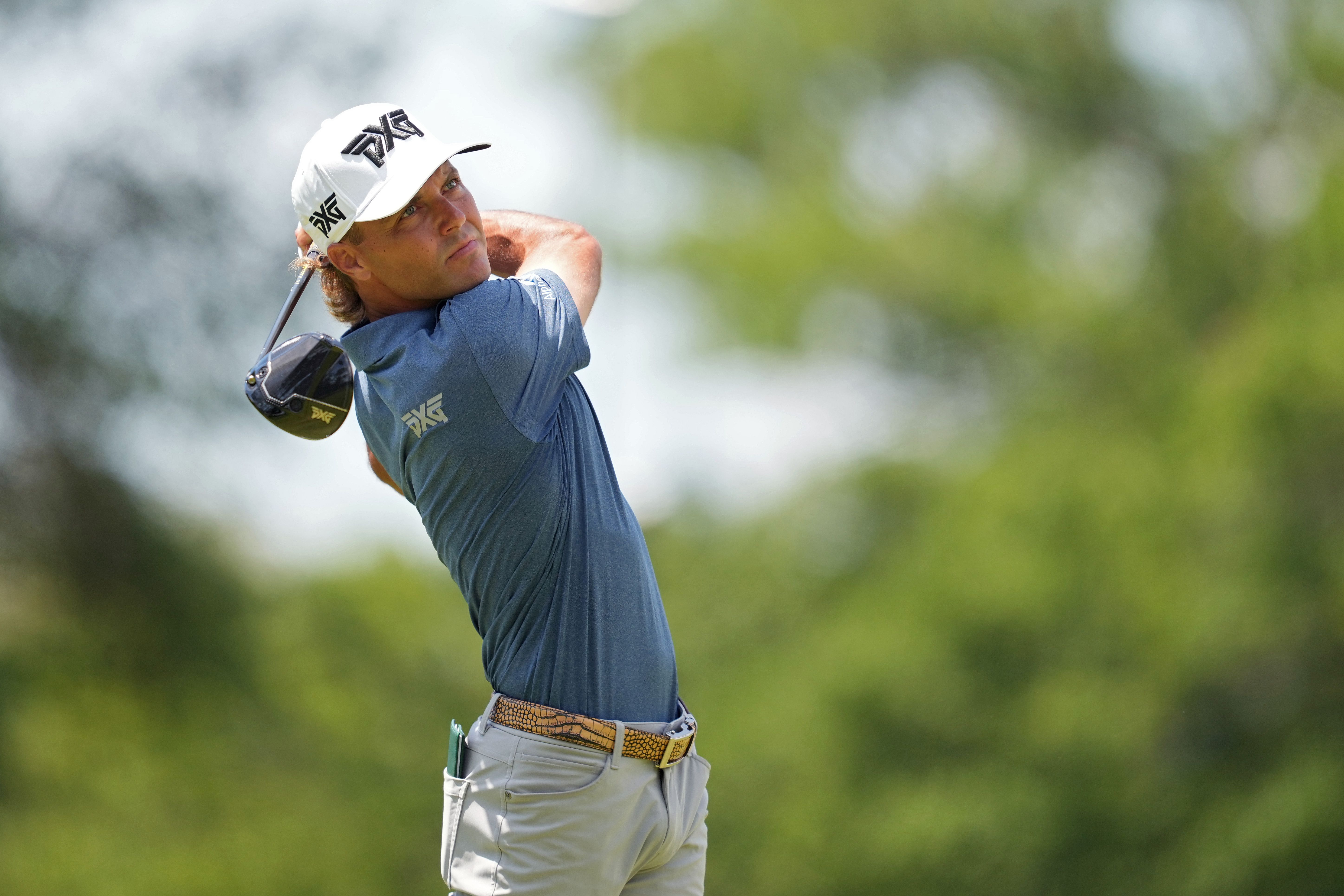 Golfer in blue shirt and white hat mid-swing on a sunny course.