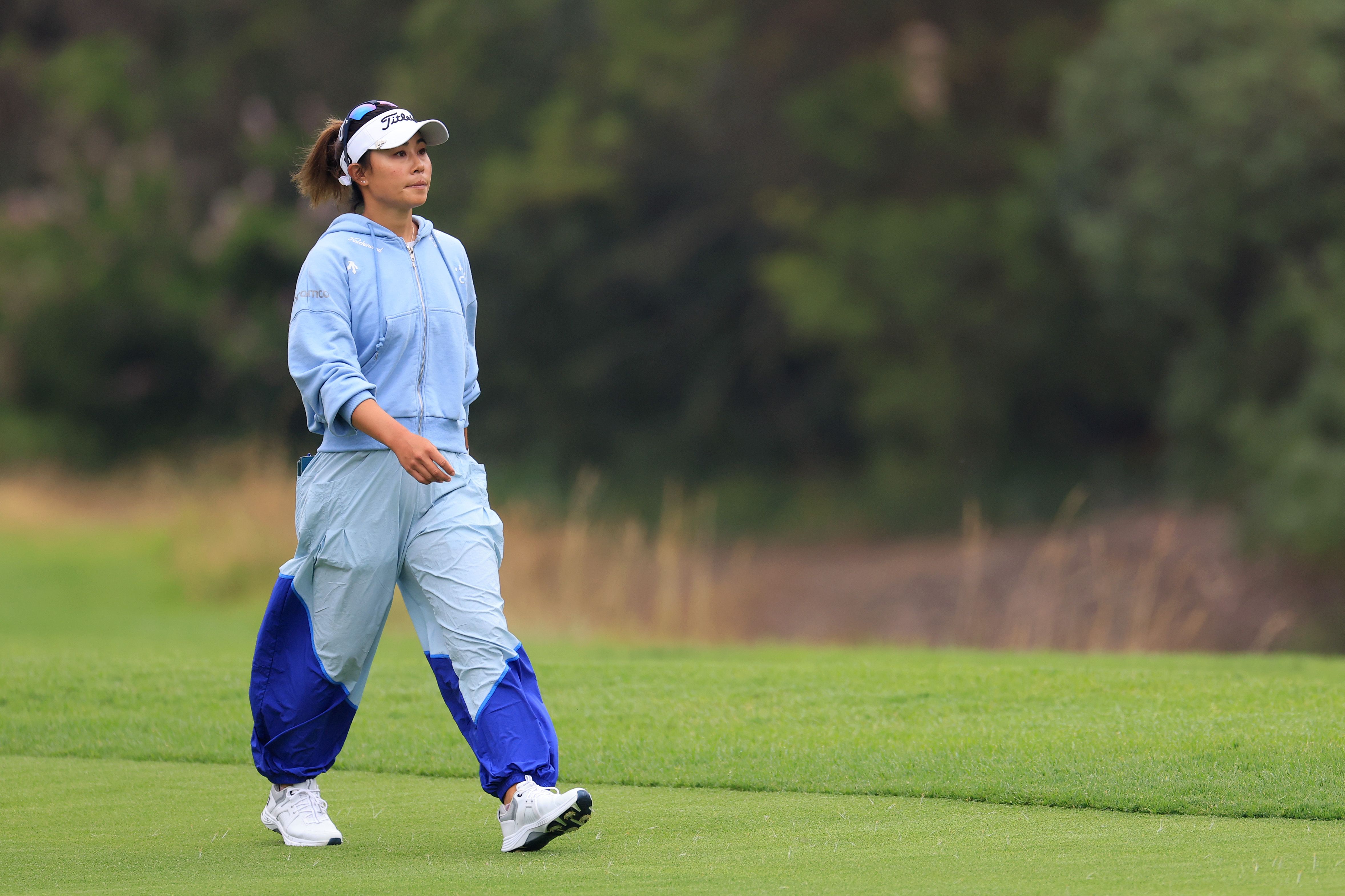 Woman in light blue golf attire walks on a green course, looking up.