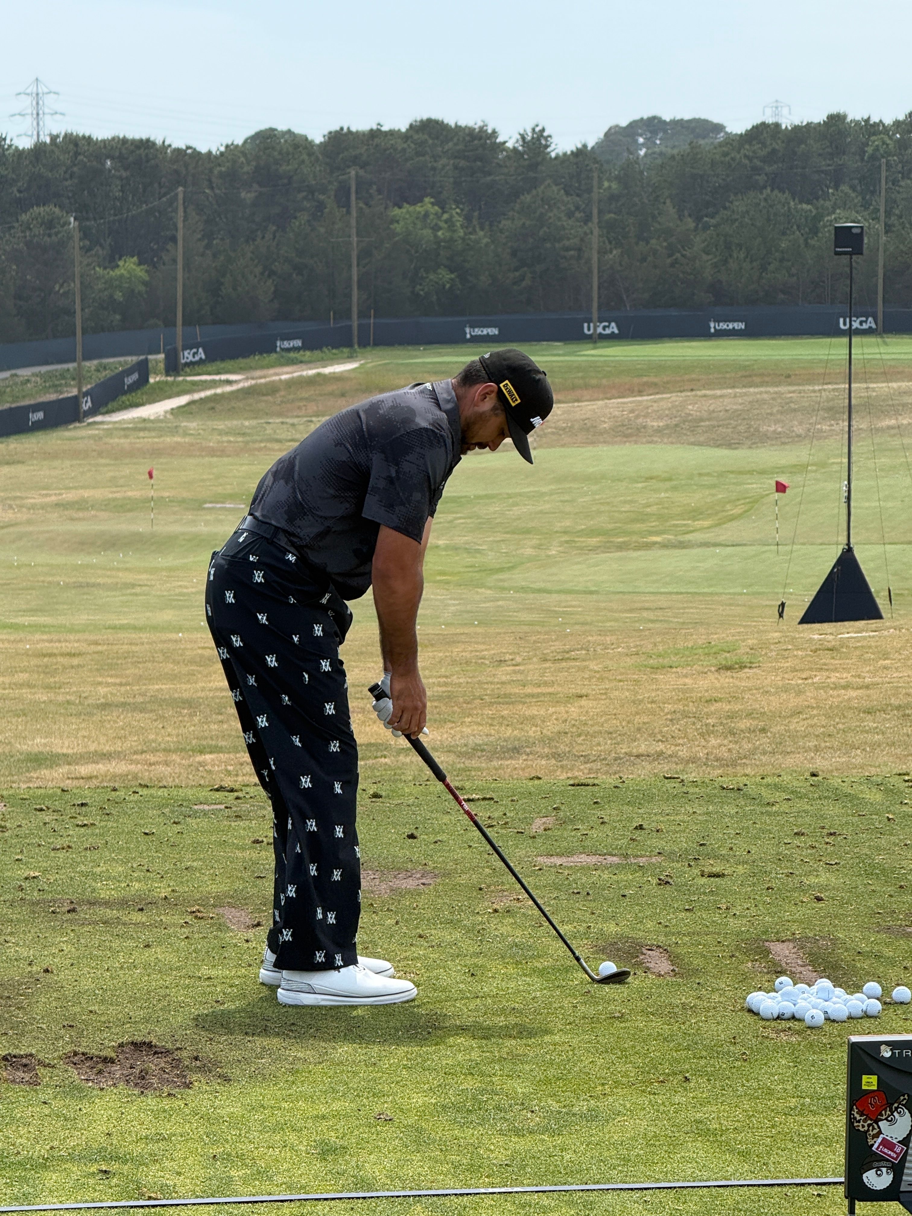 Man in patterned golf attire addresses a golf ball on a driving range.