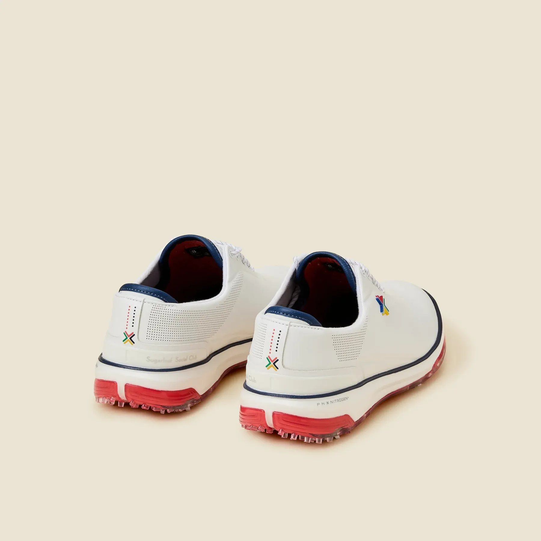 A pair of white slip-on canvas shoes with red soles and navy trim, viewed from the back.