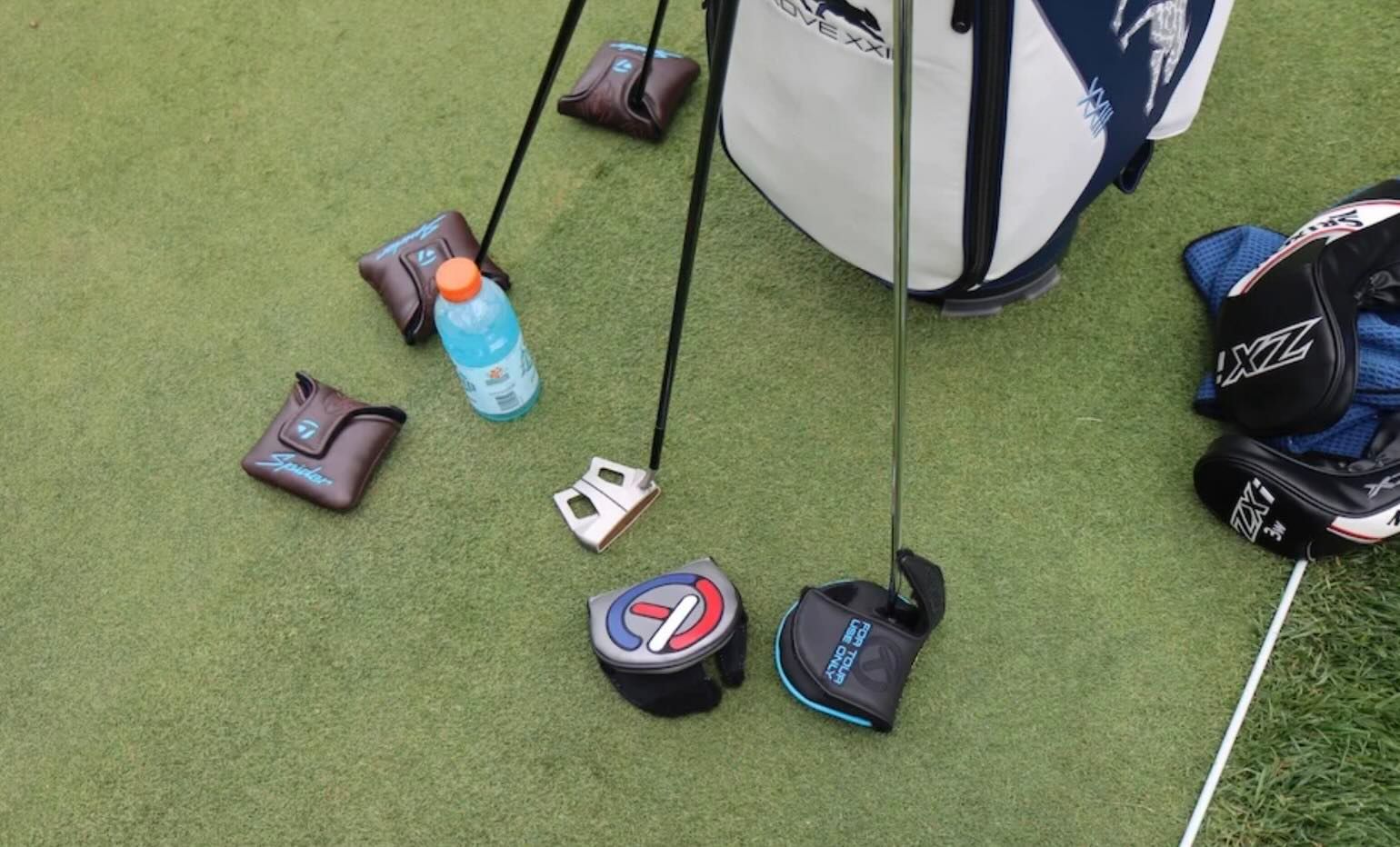 Several golf clubs, a golf bag, and a blue bottle scattered on a green golf course.