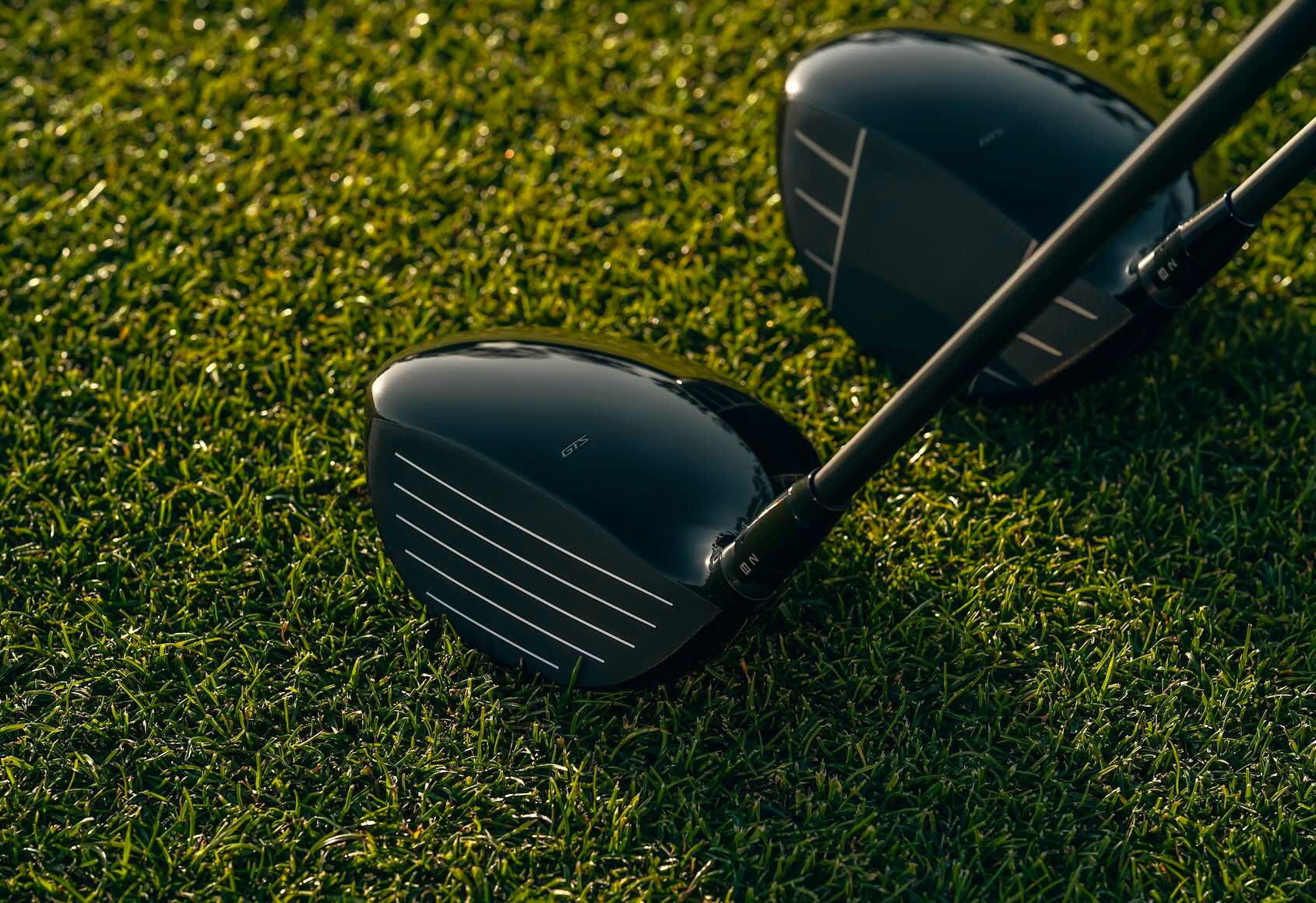 Two black golf club drivers resting on vibrant green golf course grass.