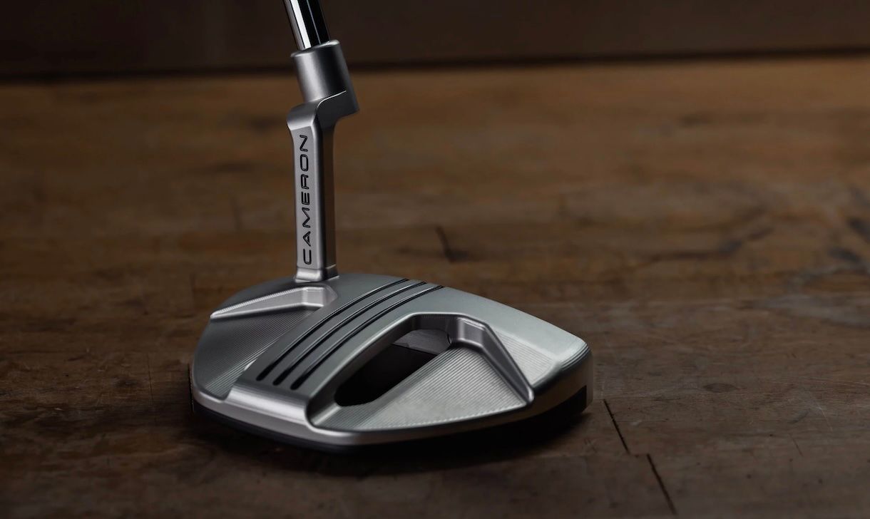 Modern silver golf putter head with angular design resting on a dark textured surface.