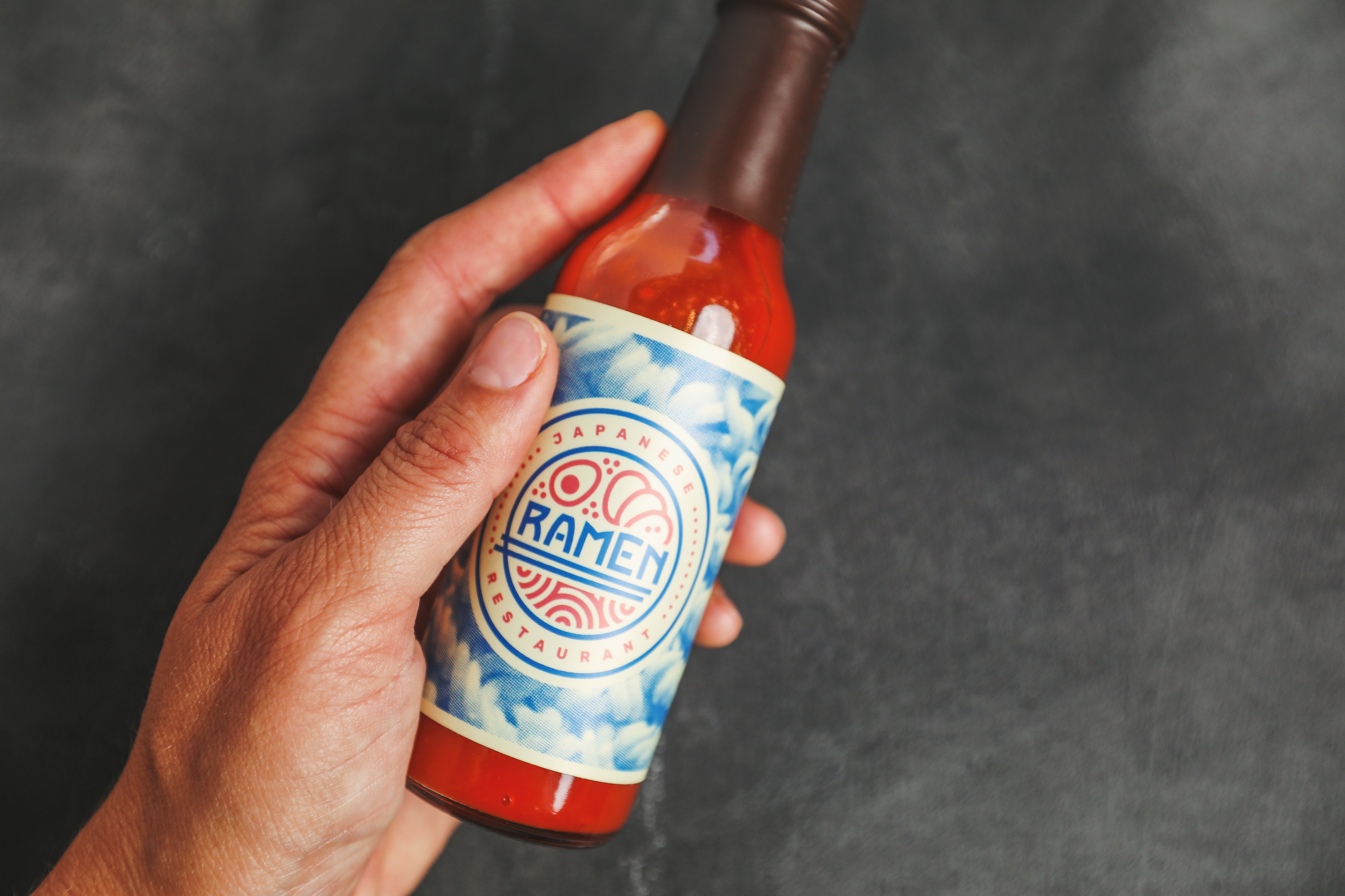 main tenant une bouteille de sauce piquante en marque blanche avec le nom de la marque de ramen sur l'étiquette