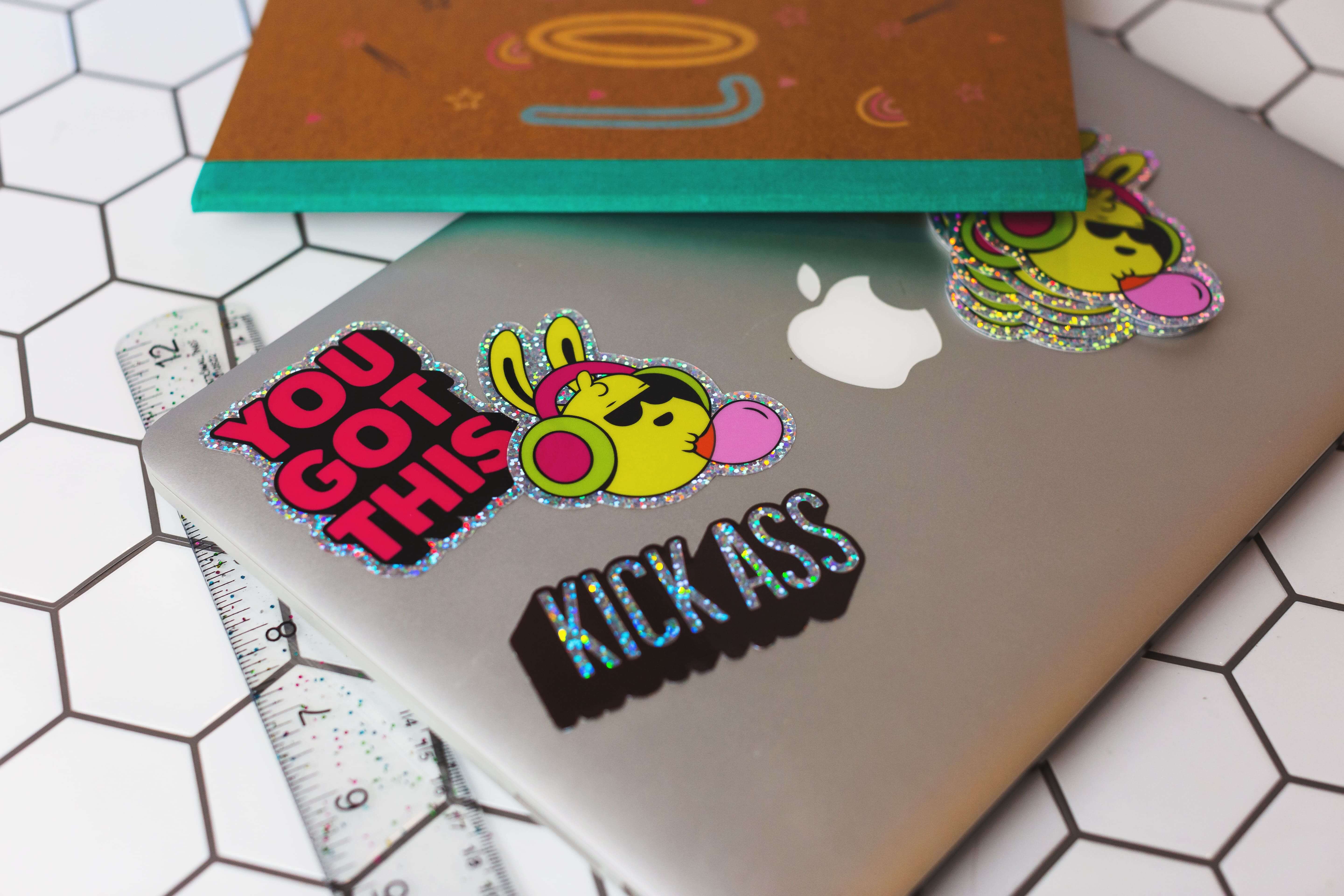 Laptop decorada con stickers troquelados holográficos coloridos, incluyendo diseños tipográficos y personajes de conejos.