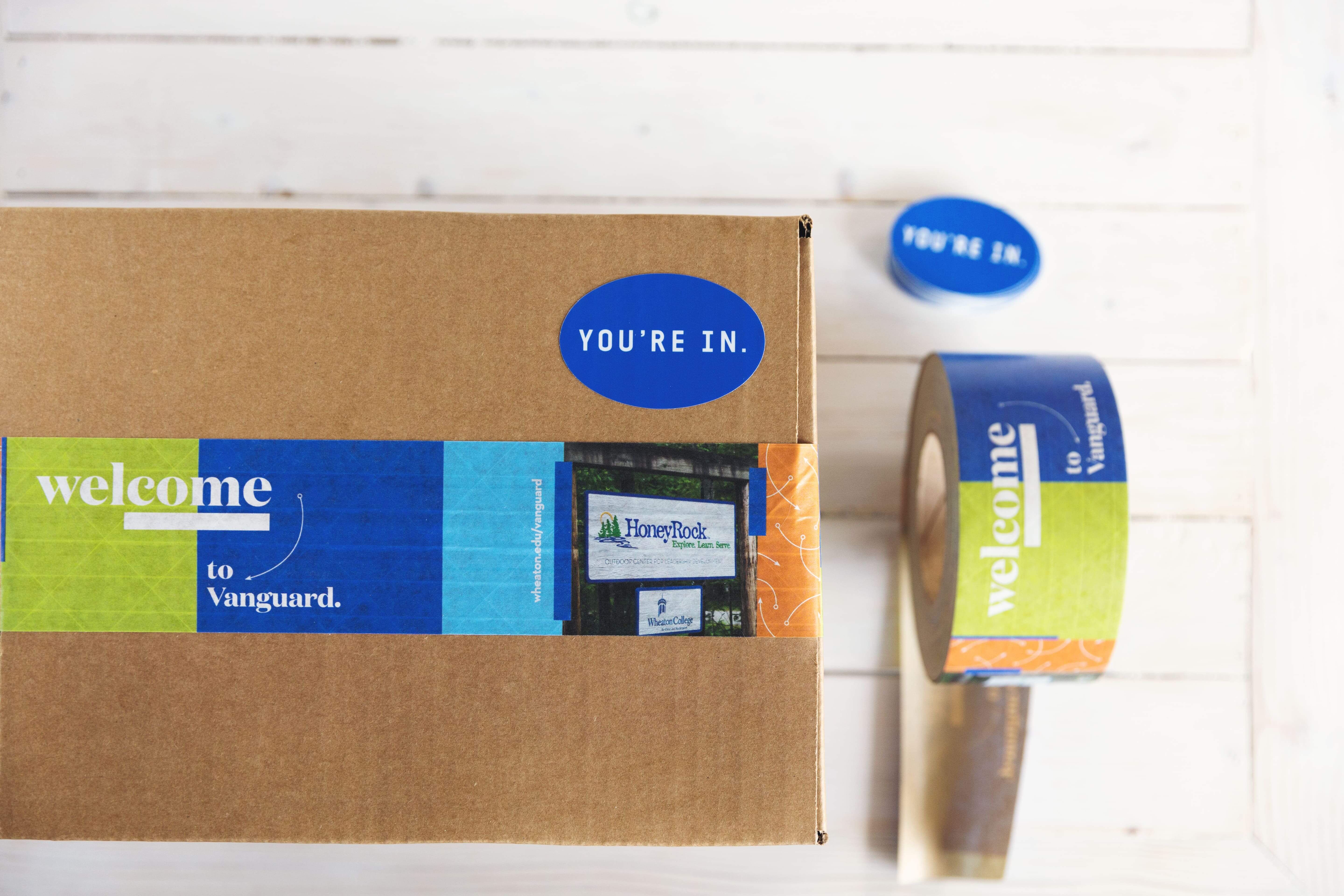 A shipping box with a blue ‘You’re in’ sticker applied to it.