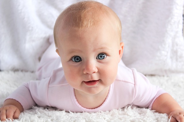 Portrait d'un bébé aux yeux bleuxs, de face, couché sur le ventre sur un tissu blanc.