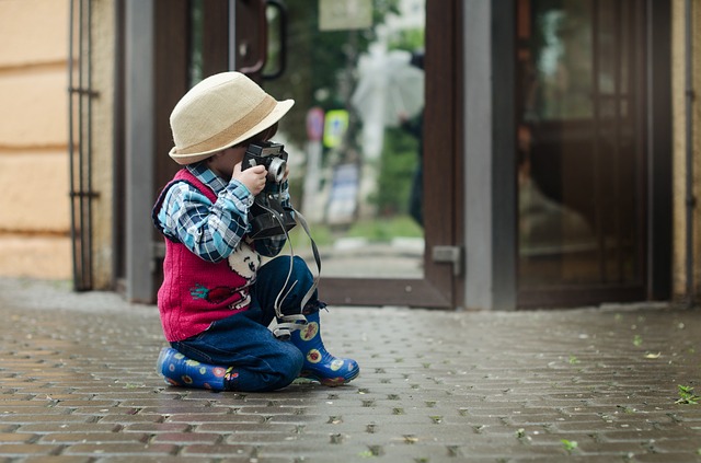 Enfant assis par terre avec un appareil photo en main, prêt à photographier.