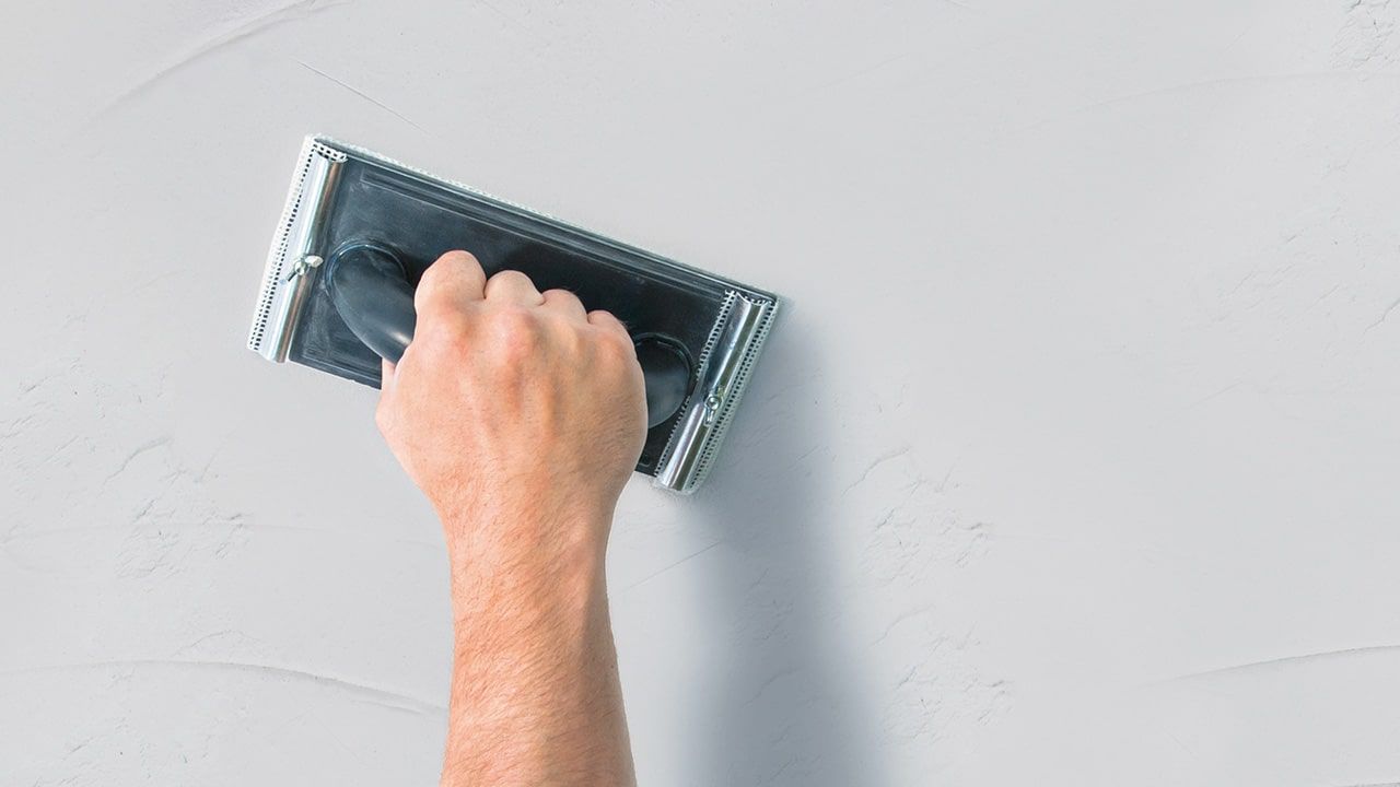 Szlifowanie ręczne szlifierką z papierem ściernym jasnoszarej ściany
