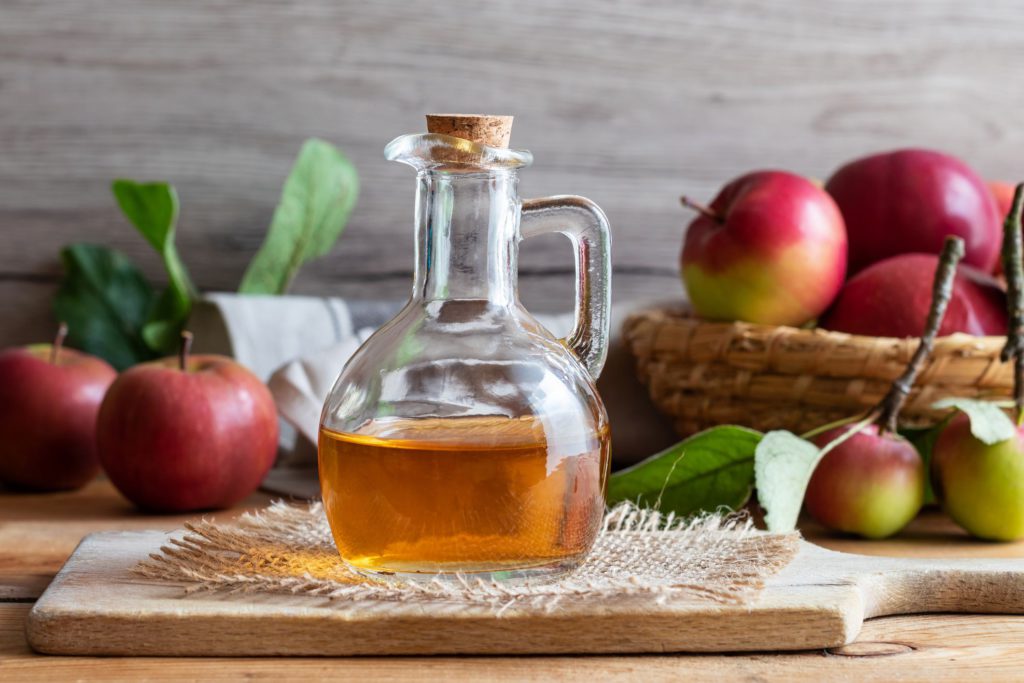 a glass jar with a liquid in it next to apples and a basket of apples