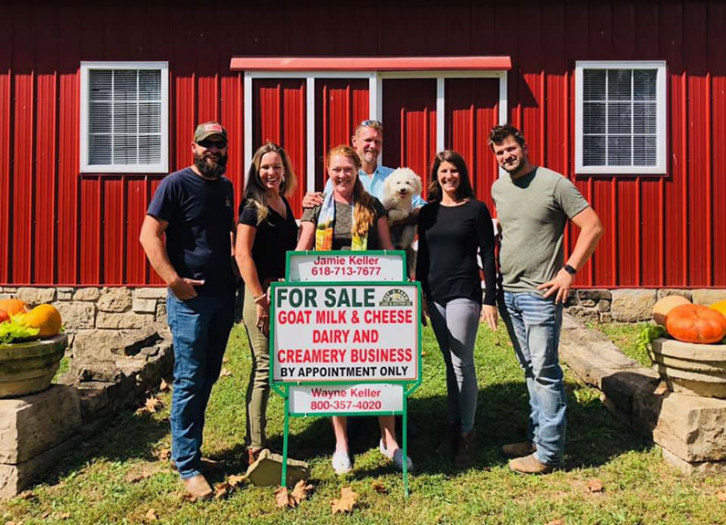 a group of people standing in front of a barn with a for sale sign